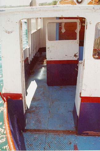 Photo of the opening in bridge front with stove-in door forced inside superstructure and unpainted, corroded foot print on main deck of missing door sill