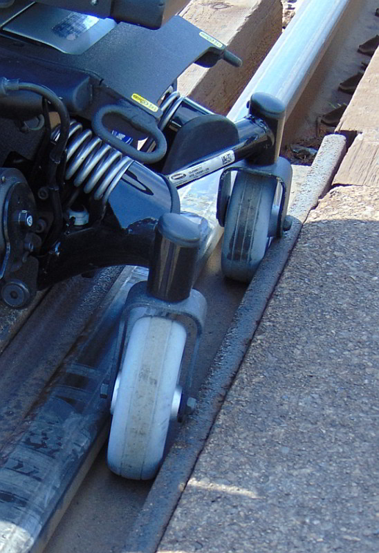   Roulettes arrière d'un    exemplaire de référence du fauteuil roulant, coincées dans l'ornière du    passage à niveau à l'étude (Source : Gendarmerie royale du Canada)